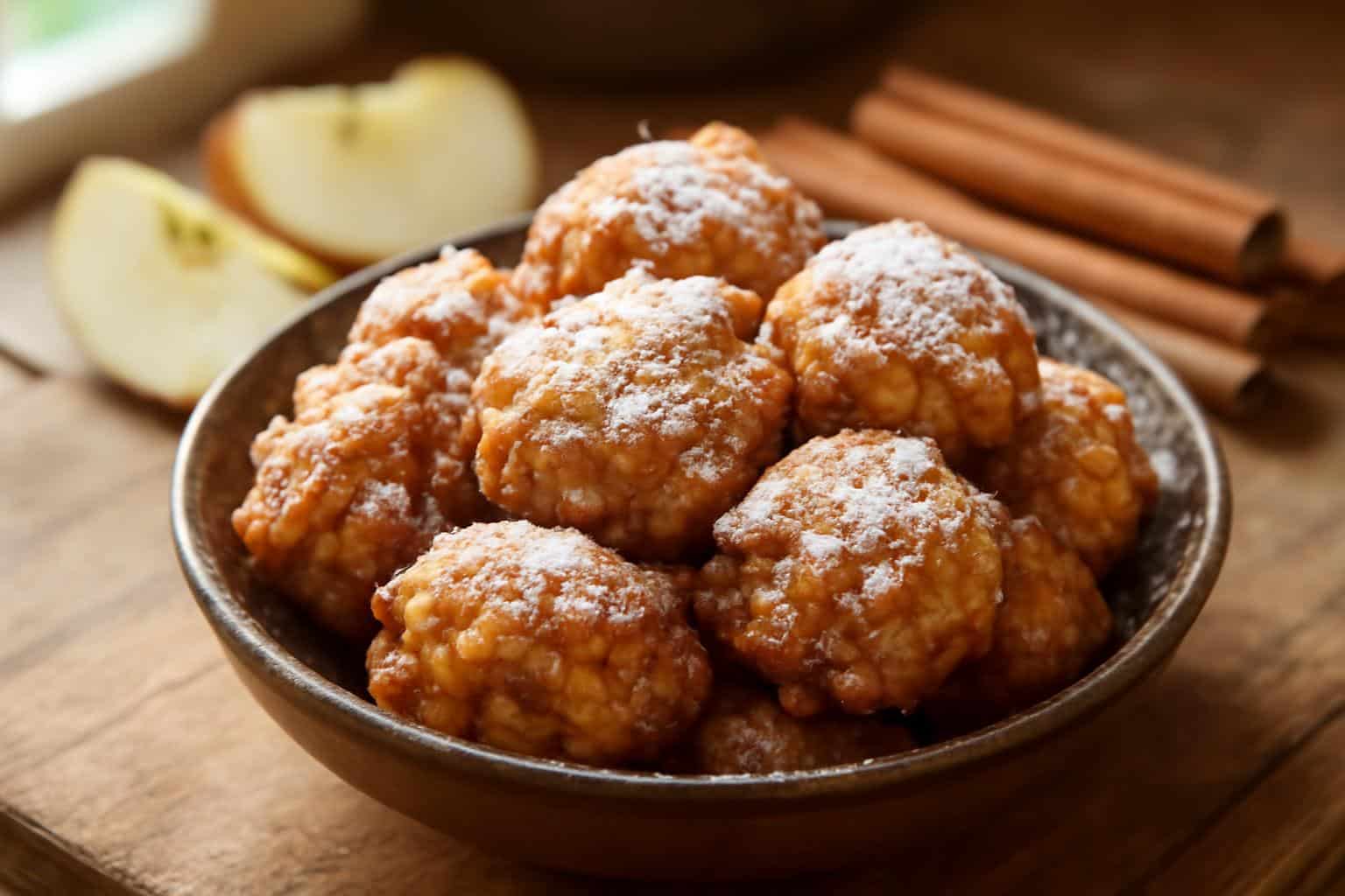 Golden apple fritter bites dusted with powdered sugar on rustic wooden surface