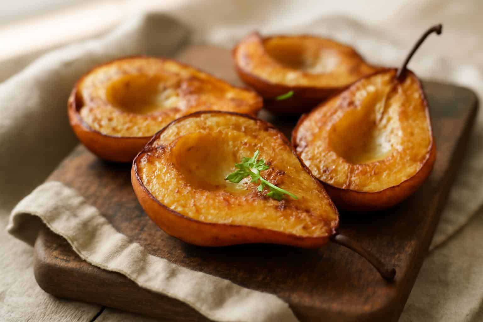 Golden buttery roasted pears with cinnamon on rustic wooden board garnished with fresh thyme