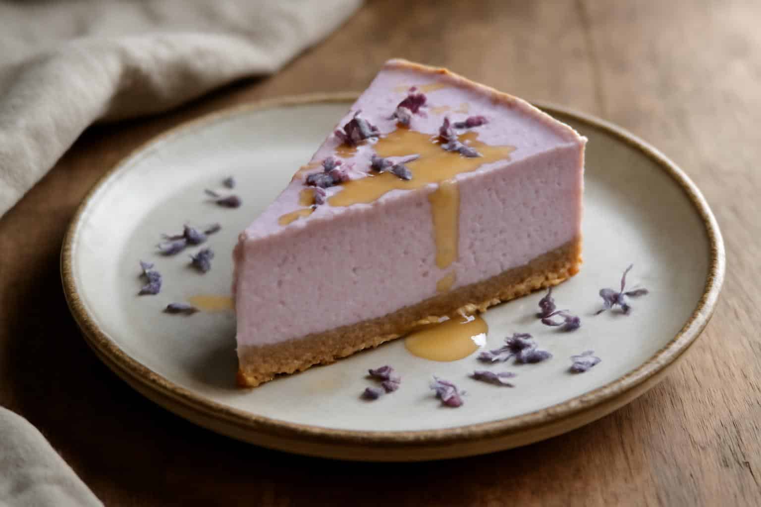 Slice of lavender cheesecake garnished with edible lavender flowers and honey drizzle