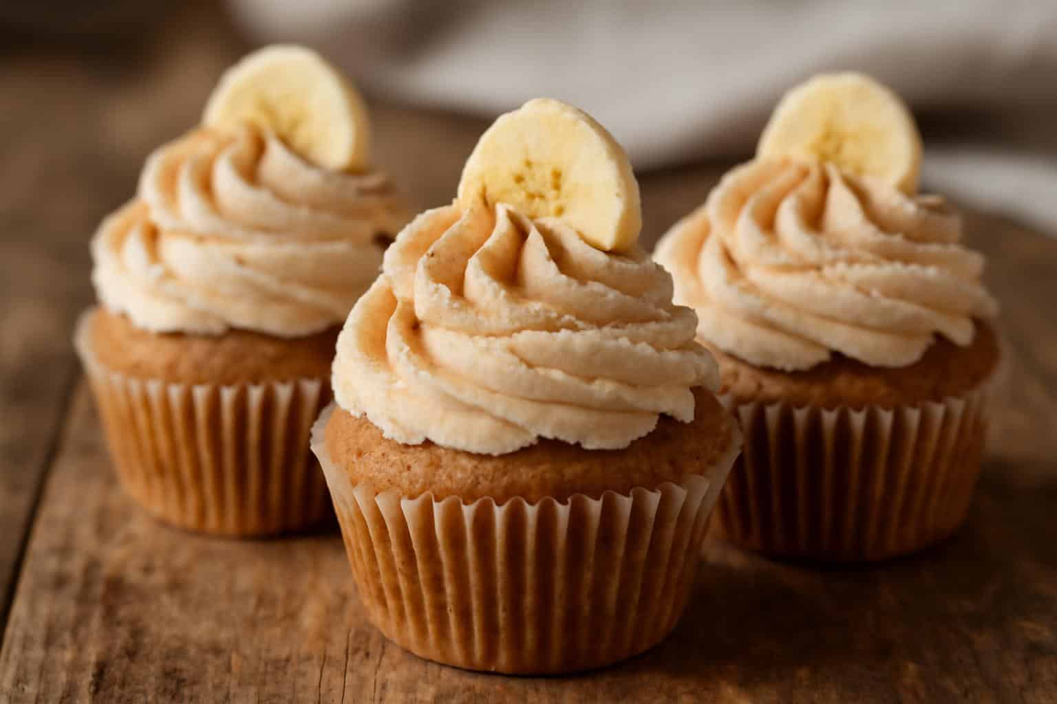 vegan banana cupcakes with cinnamon buttercream frosting on rustic wooden surface