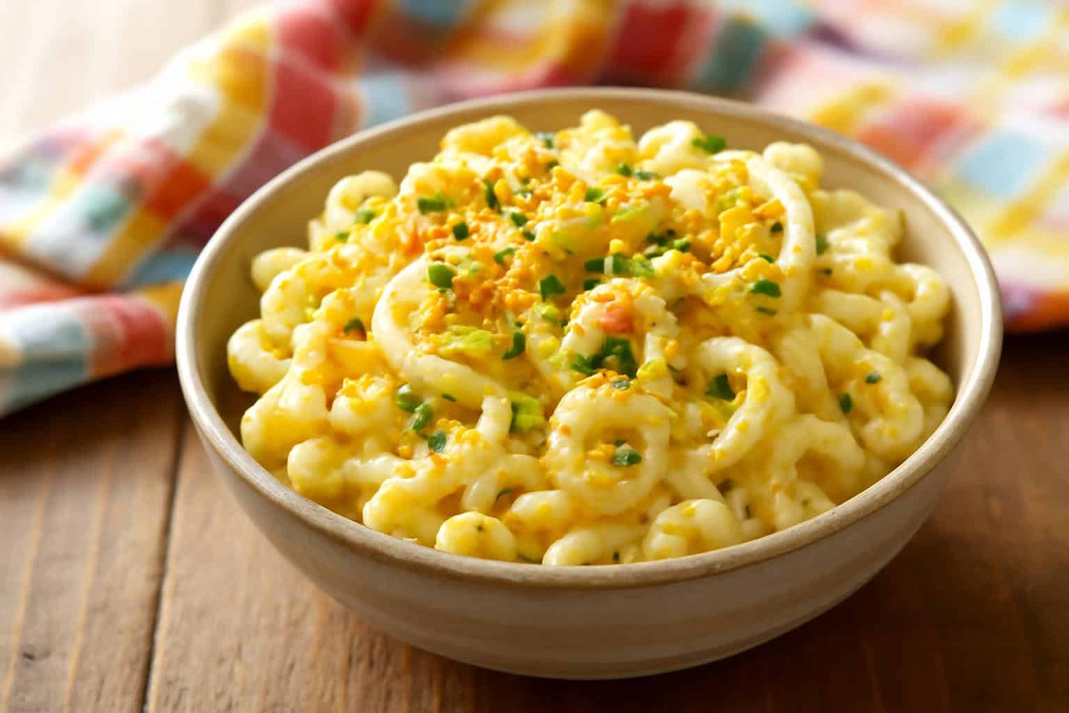 Creamy deviled egg macaroni salad garnished with chives and paprika in rustic bowl