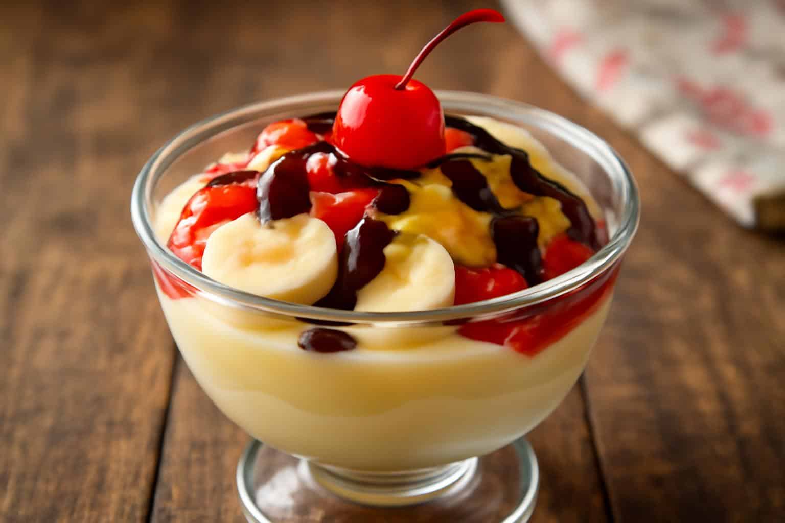 No-bake banana split dessert in glass bowl with sliced bananas, toppings, and chocolate drizzle