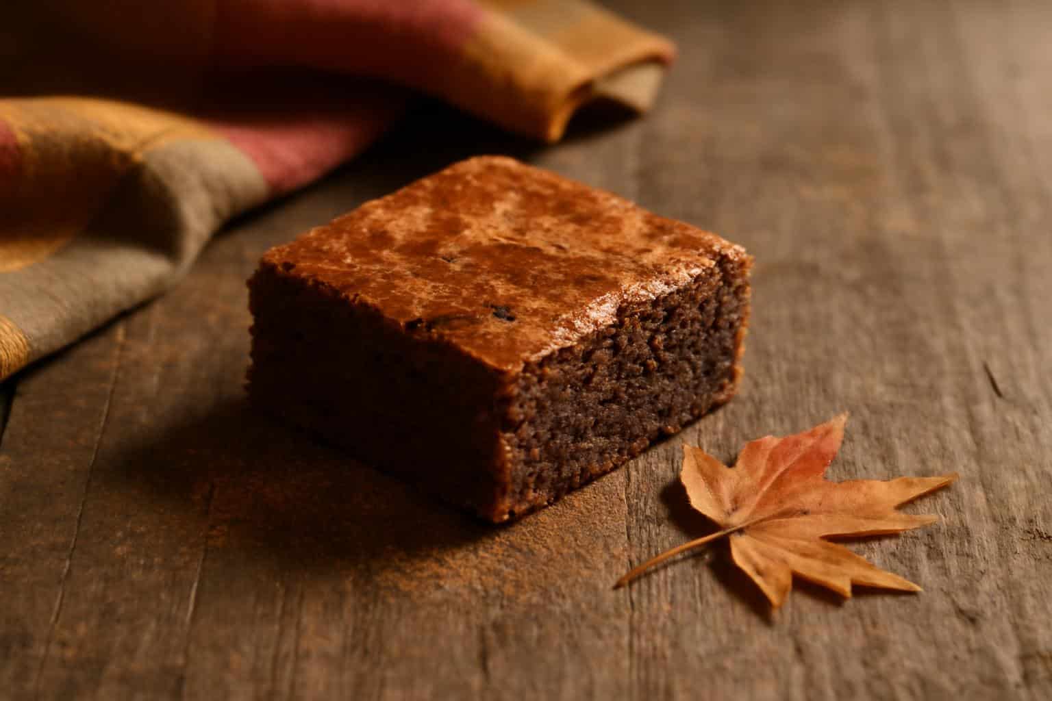 A moist maple cinnamon brownie with a crackled top and cinnamon dusting on a rustic wooden surface, showcasing maple cin