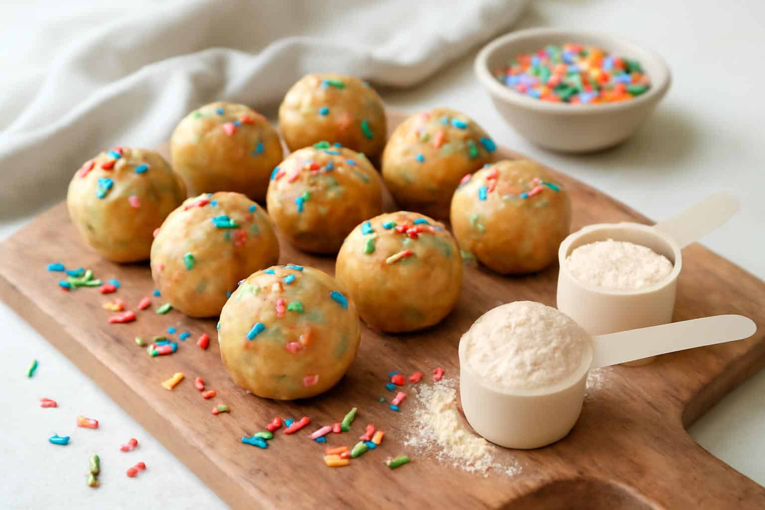 No bake cake batter protein balls with colorful sprinkles on a rustic wooden board, a high-protein snack